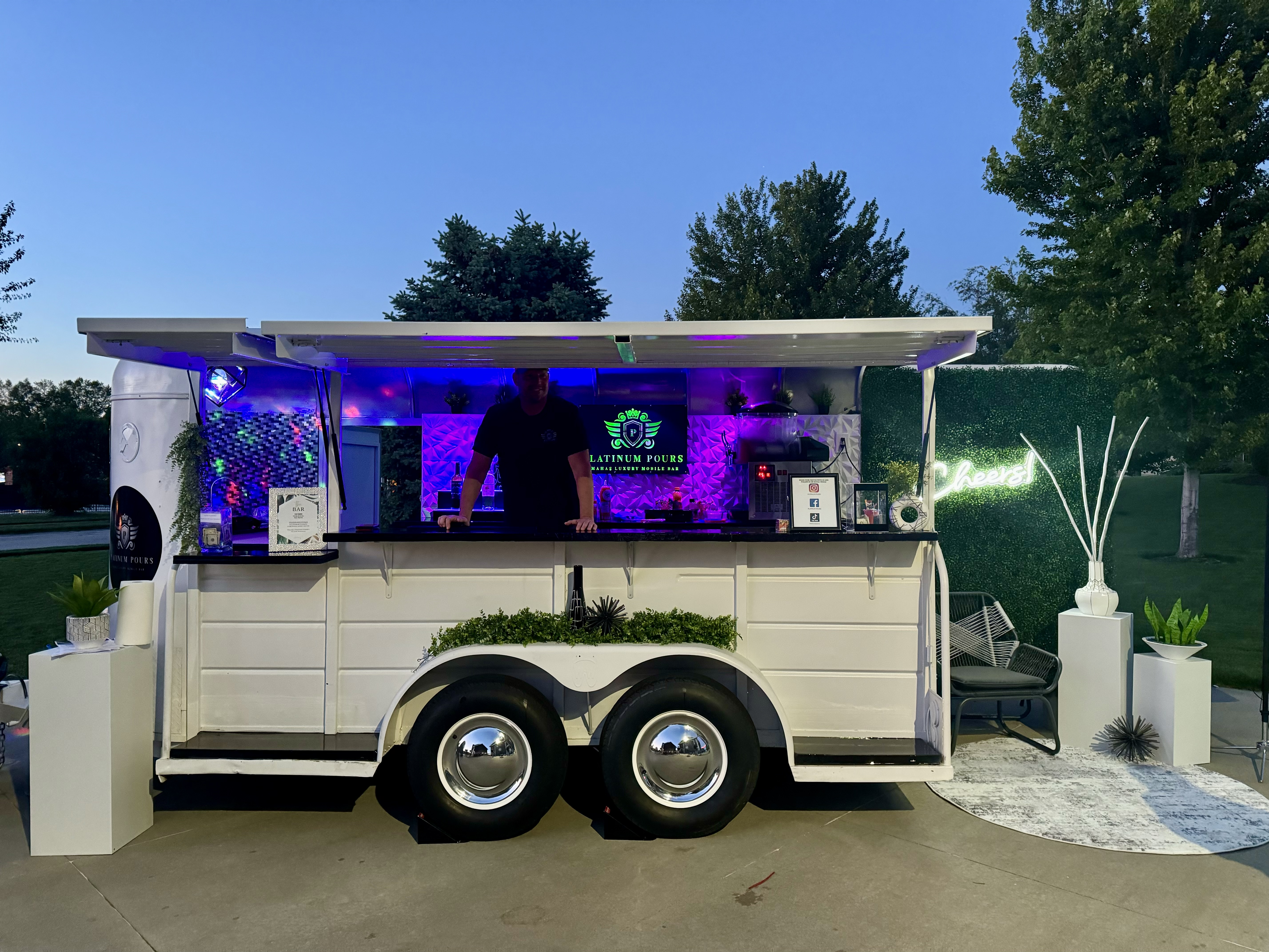 Jackpot, the Platinum Pours luxury mobile bar trailer at golden hour with LED interior glow and Cheers neon wall