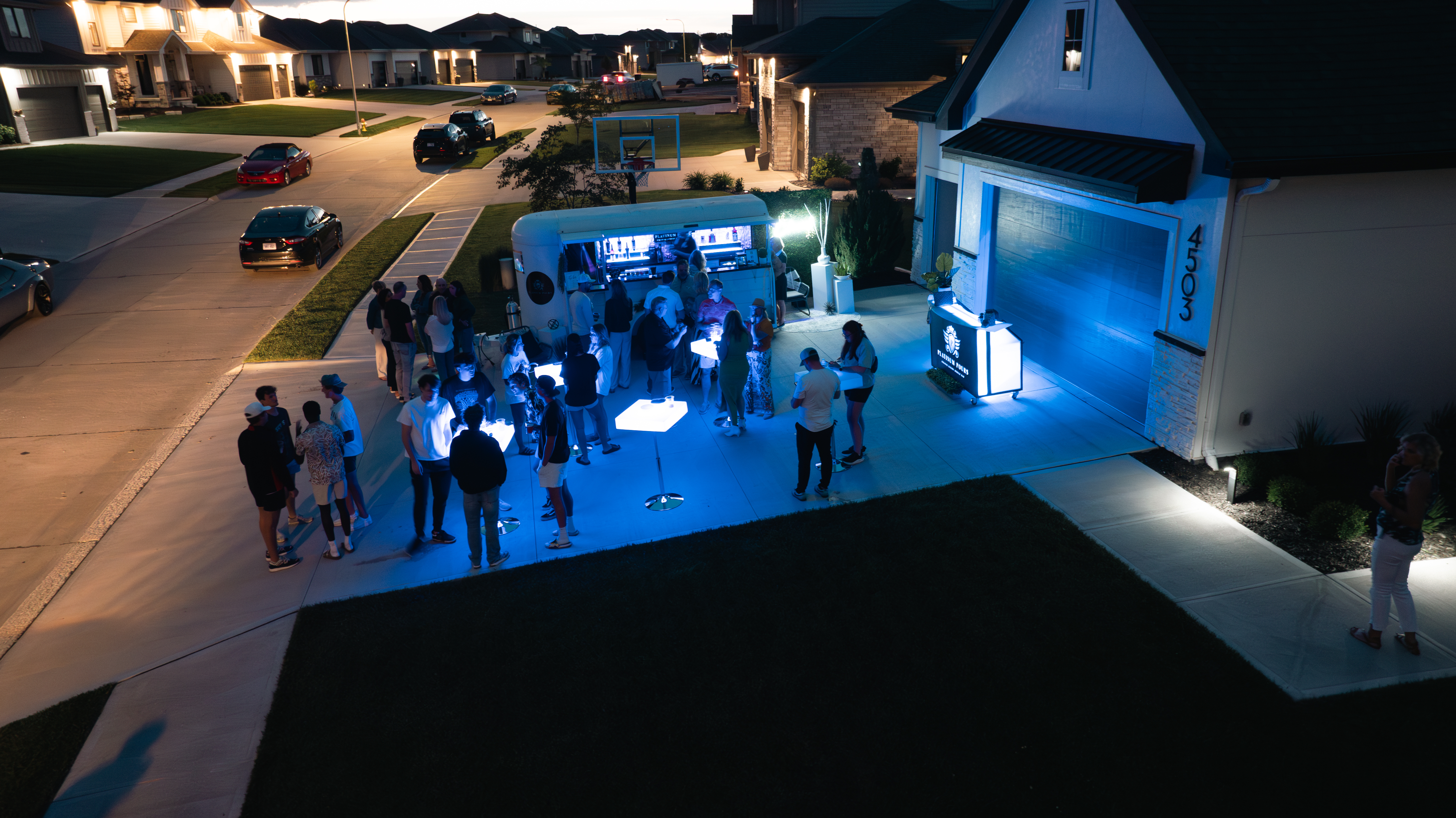 Aerial view of a private driveway party at night with Platinum Pours mobile bar, LED cocktail tables and a full crowd of guests