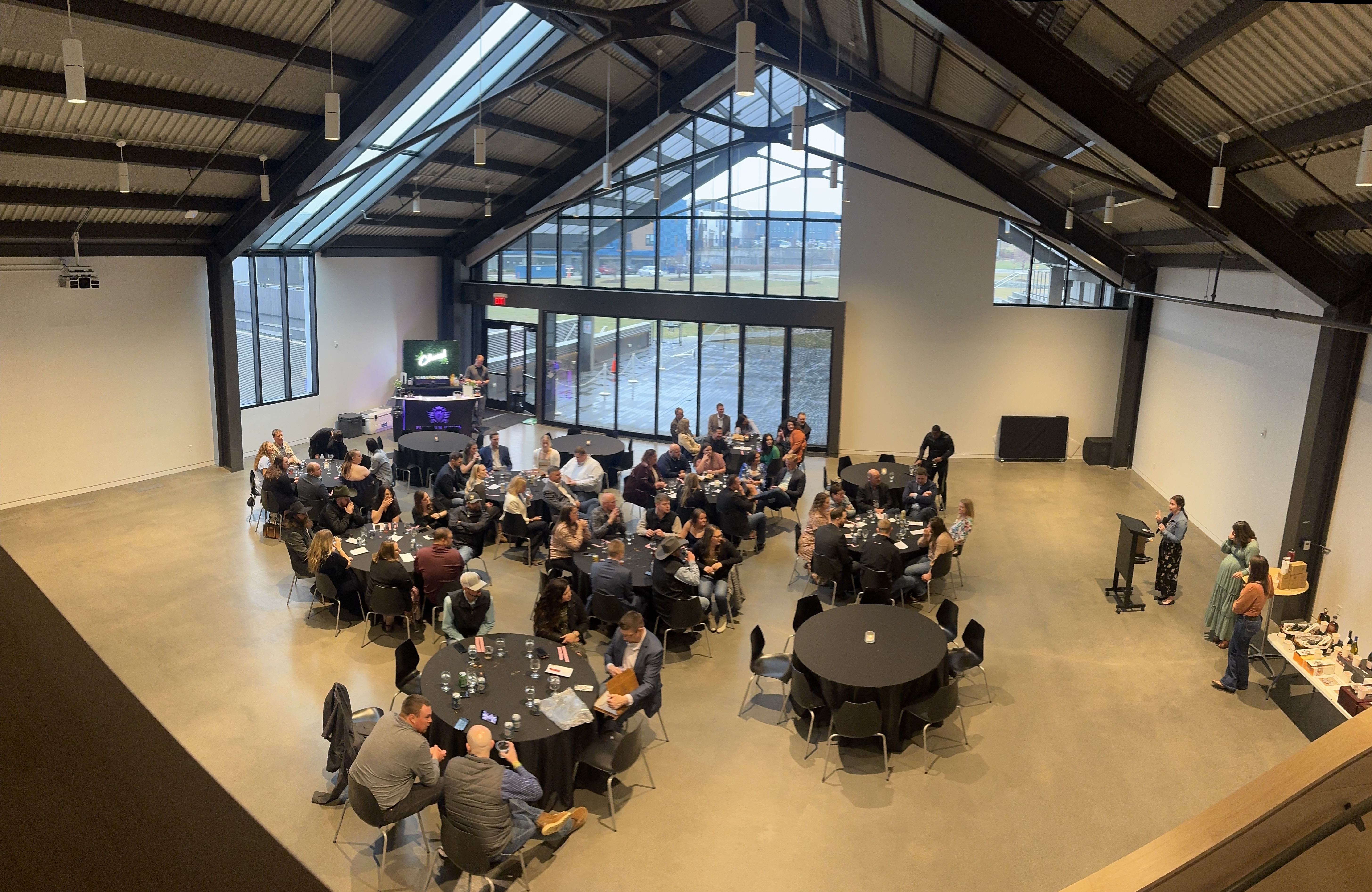 Platinum Pours bar setup at a modern industrial venue corporate dinner with full crowd seated at black round tables
