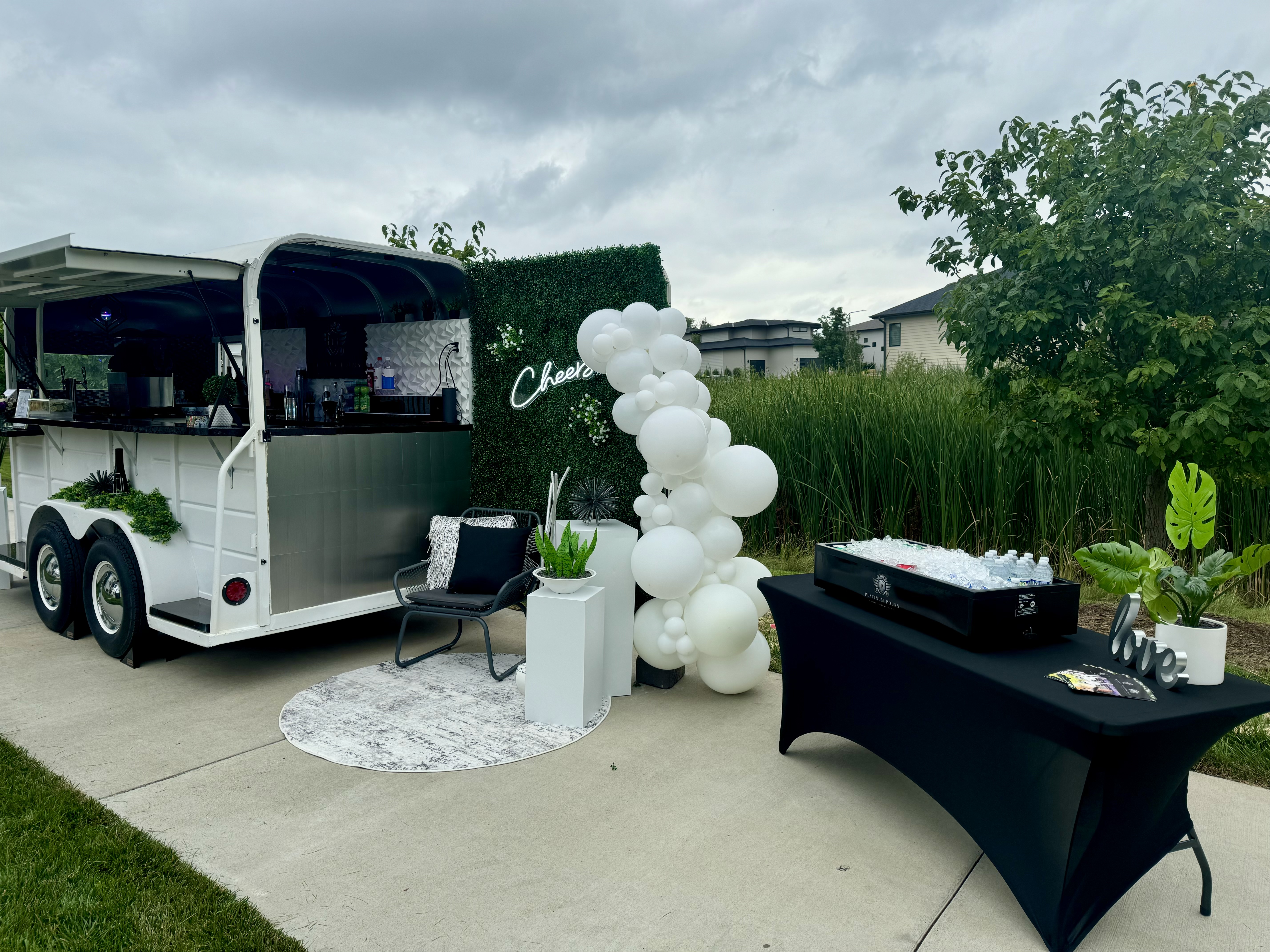 Platinum Pours wedding setup with Jackpot mobile bar, white balloon arch, branded ice tub and Cheers neon wall