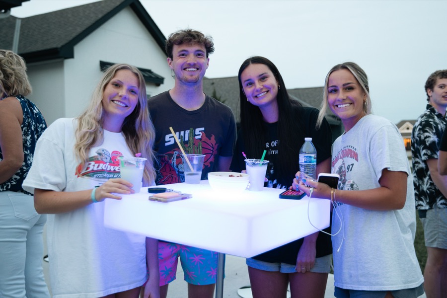 Four friends gathered around a glowing white LED cocktail table at sunset