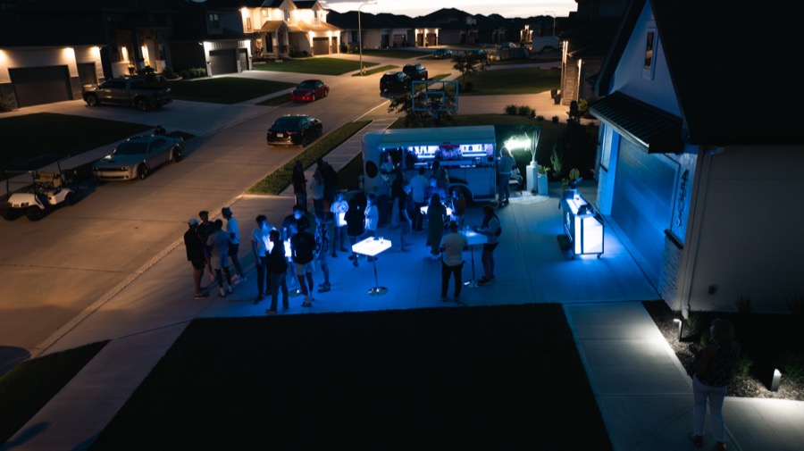 Aerial view of an evening driveway party with the Jackpot bar lit up and LED cocktail tables glowing across the crowd