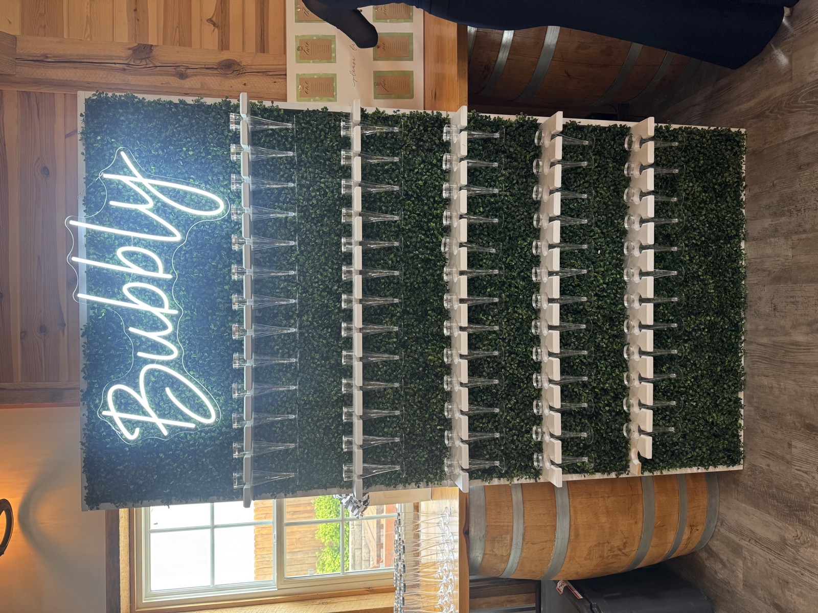 Boxwood Champagne wall with Bubbly neon sign and rows of disposable flutes