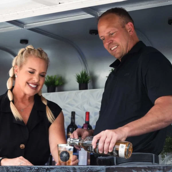 Allie and Scott, owners of Platinum Pours, pouring a drink for a guest at their 2024 launch party in Omaha, NE, featuring their mobile bar trailer.